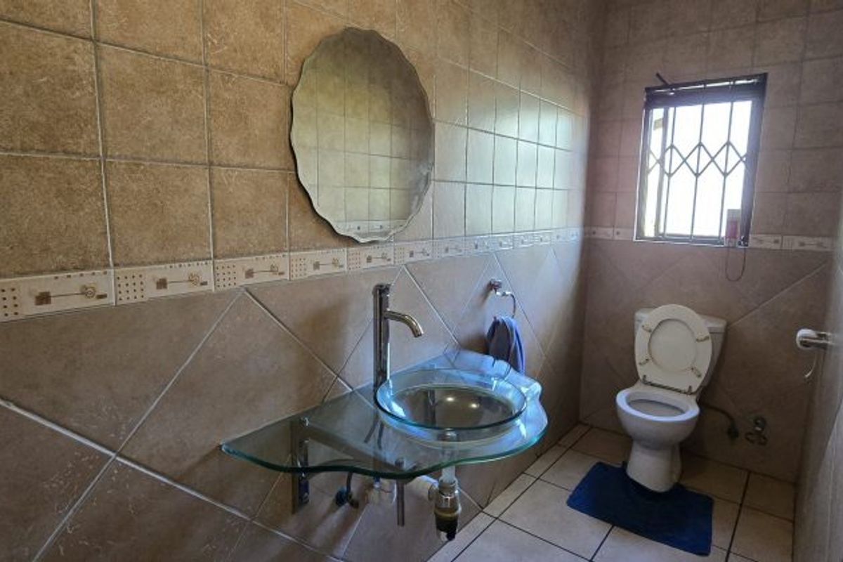 A functional bathroom featuring a glass vessel sink, wall-mounted faucet, and full-height ceramic wall tiling with a decorative border.