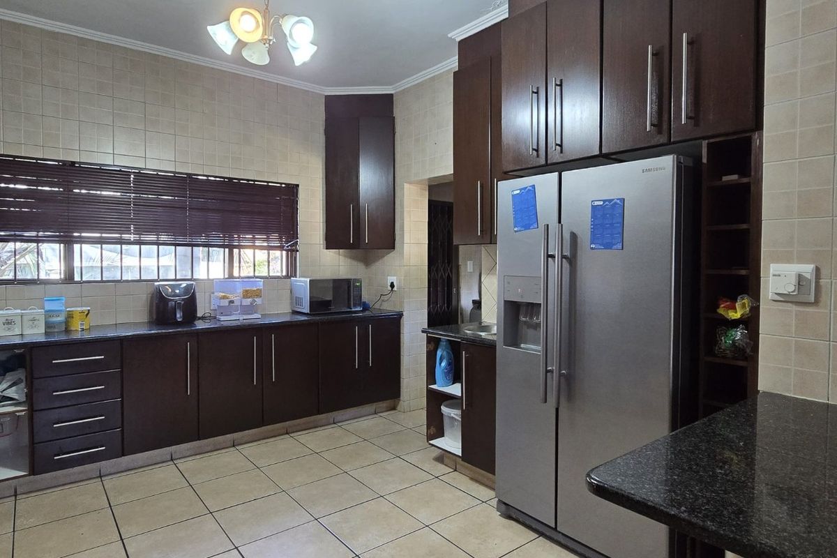 A functional kitchen featuring dark wood cabinetry, granite countertops, tiled backsplash, and tiled flooring, equipped with a built-in oven and double door refrigerator.