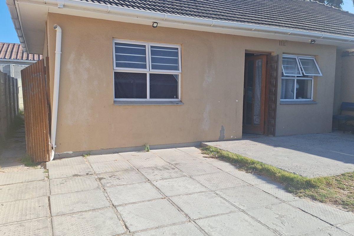 Rear exterior view of the house featuring a paved patio area, tiled roof, and security-fitted windows.