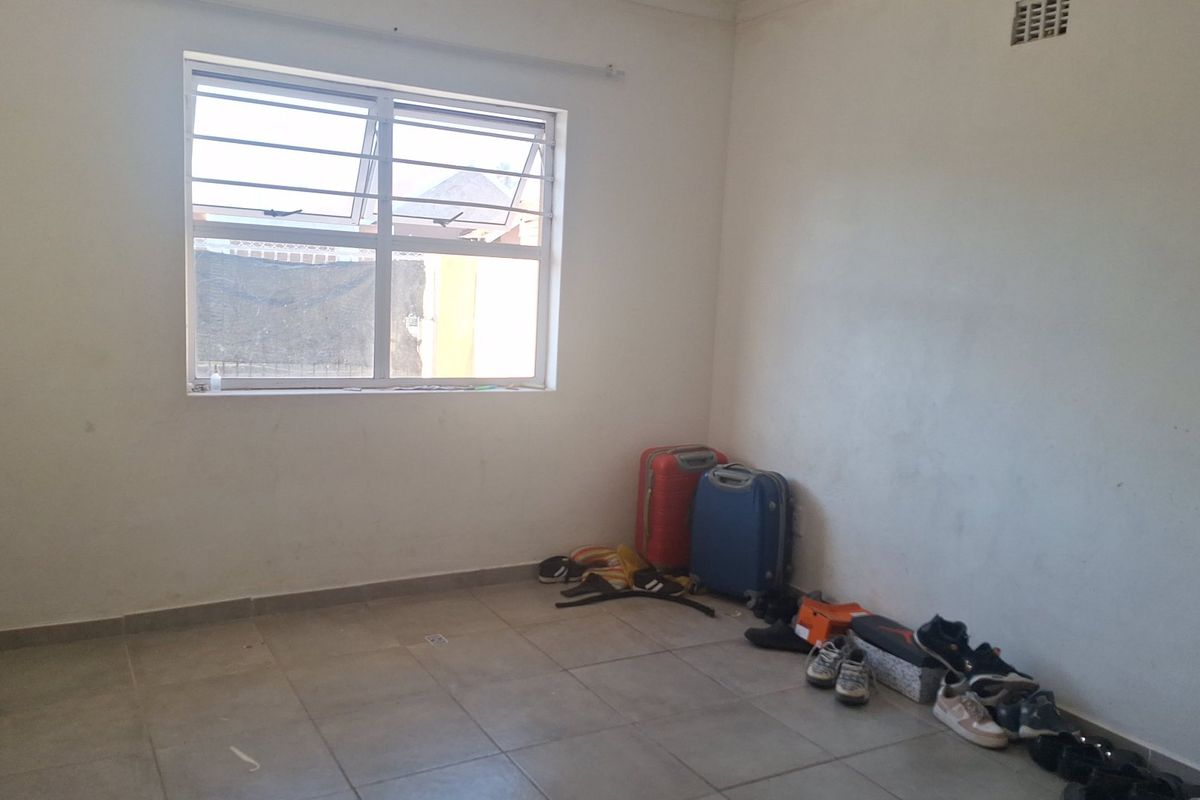 A vacant bedroom featuring tiled flooring, a window with security bars, and a wall-mounted ventilation grille.