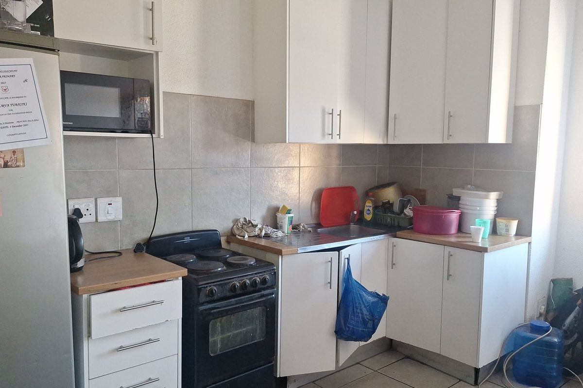 Compact kitchen featuring white cabinetry, tiled backsplash, stainless steel sink, and a freestanding stove with a dedicated microwave shelf.