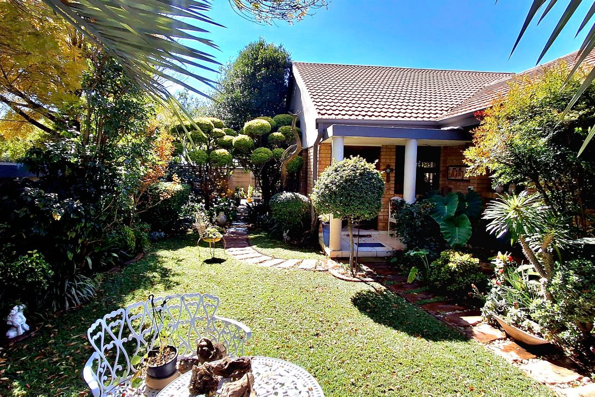 A well-maintained rear garden featuring a stone pathway, lush landscaping, and a covered patio area attached to the brick townhouse structure.