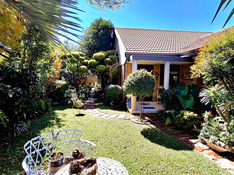 A well-maintained rear garden featuring a stone pathway, lush landscaping, and a covered patio area attached to the brick townhouse structure.