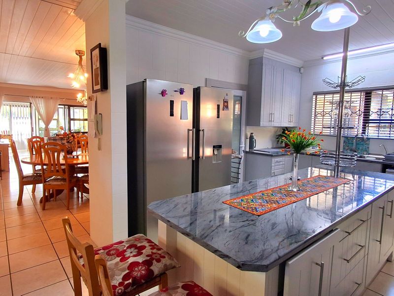Open plan kitchen and dining area featuring a central island with stone countertops, shaker cabinetry, and tiled flooring throughout.