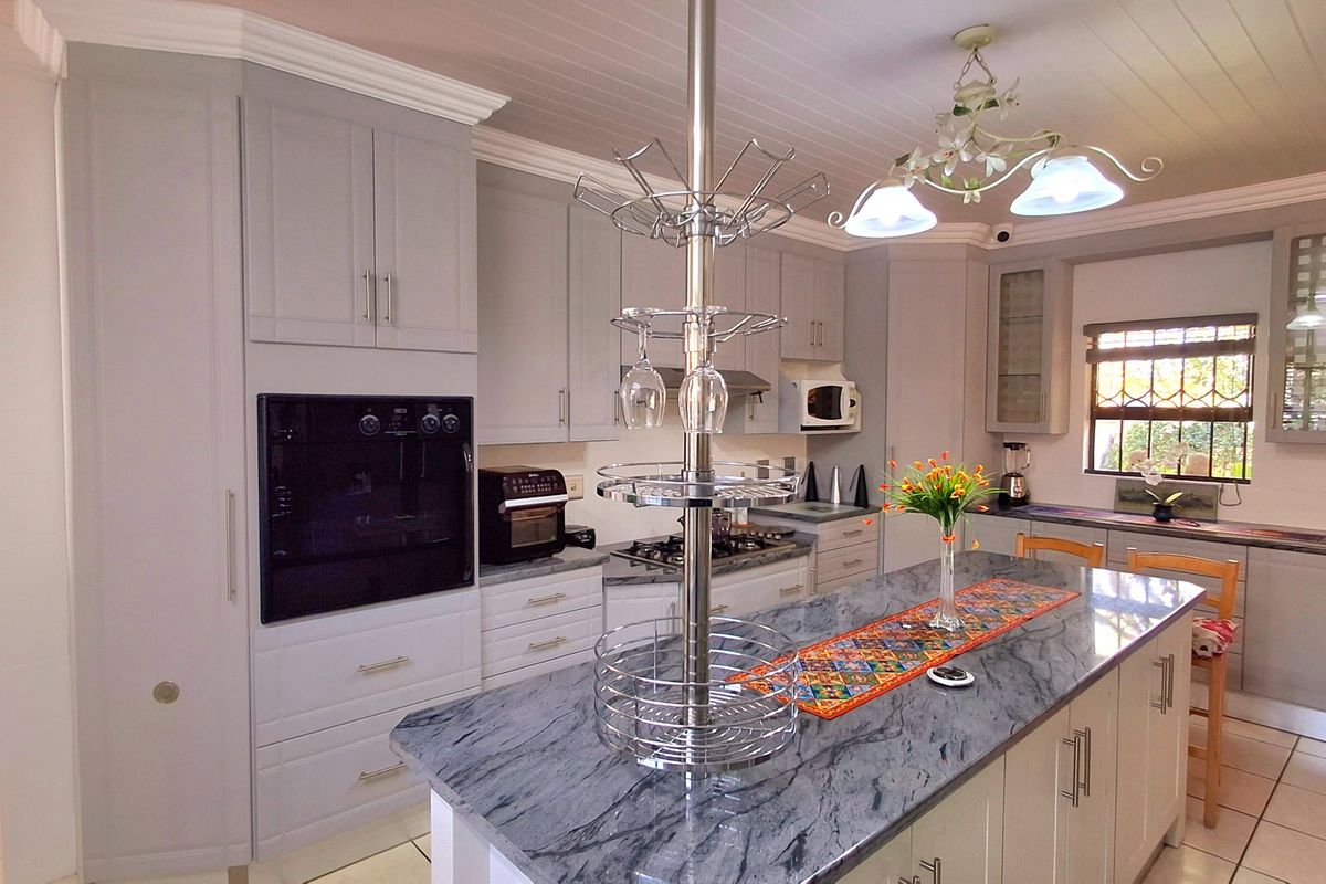 Modern kitchen featuring grey shaker-style cabinetry, a large stone-topped island, built-in oven, gas hob, and tiled flooring with a classic tongue and groove ceiling.
