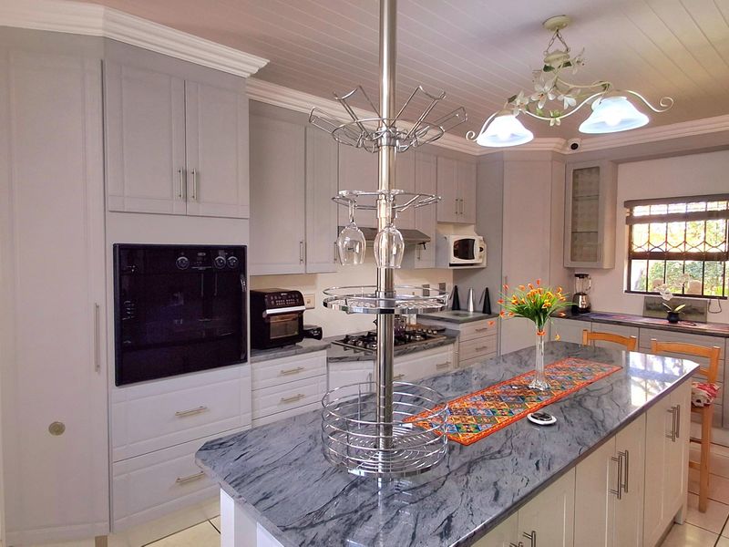 Modern kitchen featuring grey shaker-style cabinetry, a large stone-topped island, built-in oven, gas hob, and tiled flooring with a classic tongue and groove ceiling.