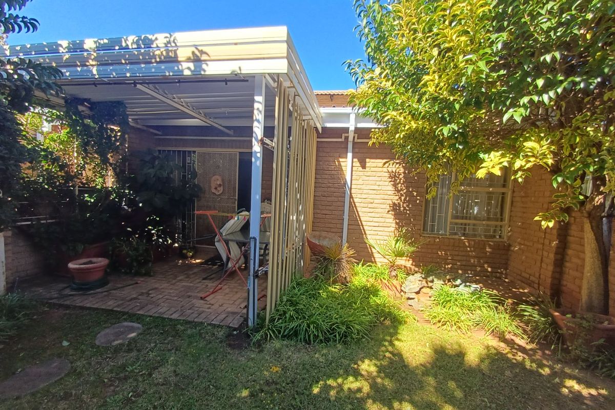 A rear exterior view of the property featuring a covered patio area with brick facade and established garden surroundings.