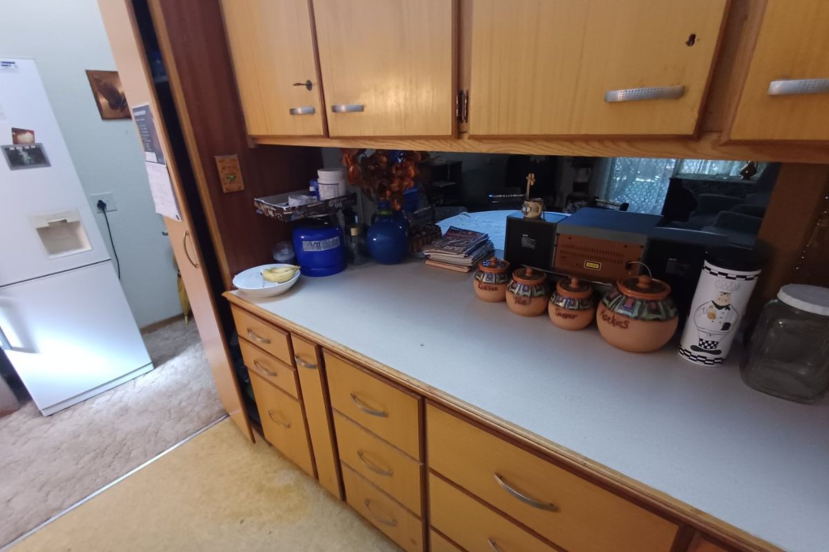 A dated kitchen area featuring wood-look laminate cabinetry, a neutral countertop, and a mirrored backsplash, offering potential for a modern renovation.