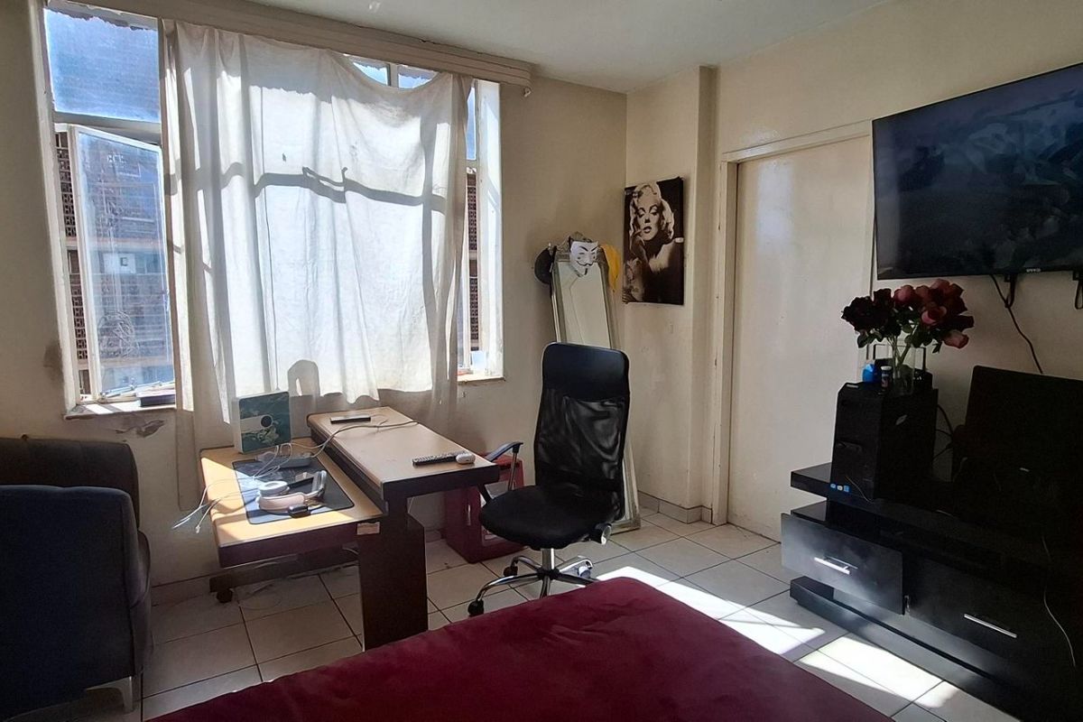 A bedroom featuring tiled flooring and a large window, currently showing signs of wear and requiring cosmetic updates to the walls and window area.