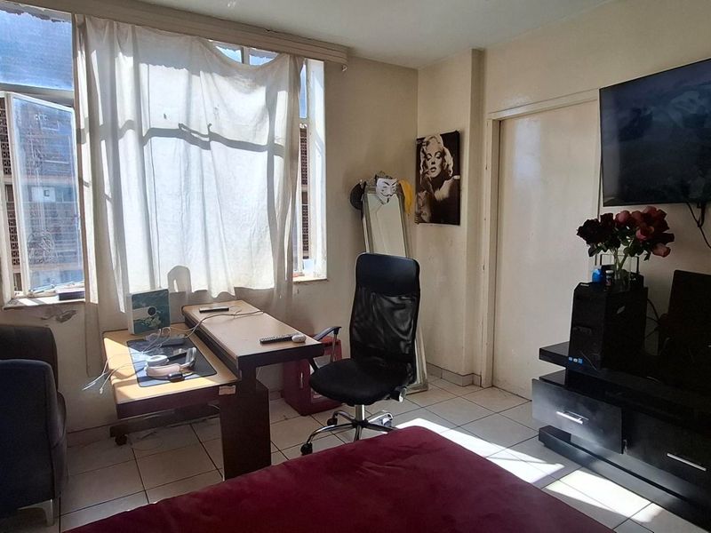 A bedroom featuring tiled flooring and a large window, currently showing signs of wear and requiring cosmetic updates to the walls and window area.
