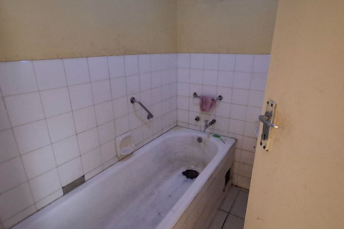 A dated bathroom featuring a built-in bathtub with tiled splashbacks and a grab rail, requiring renovation and cosmetic updates to improve its condition.