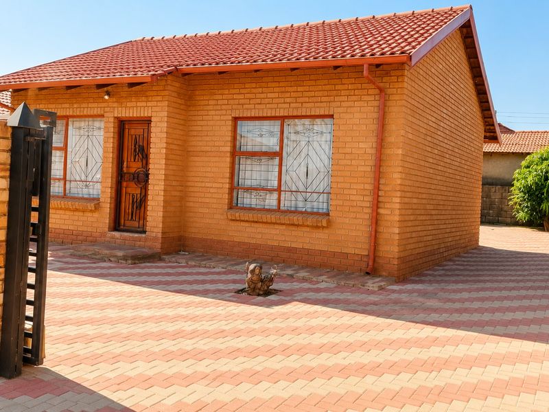A well-maintained face brick house featuring a tiled roof, paved driveway, and secure entrance with burglar bars.