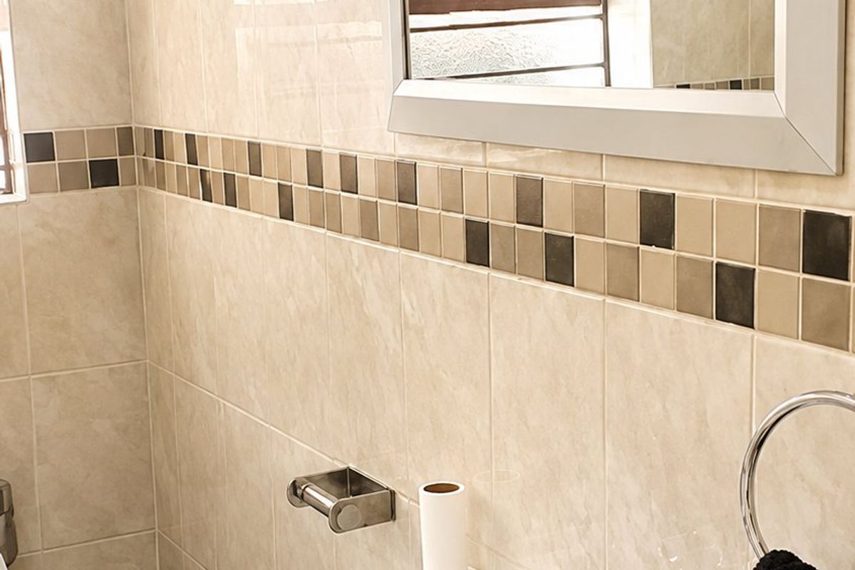 A functional bathroom featuring a pedestal basin, chrome fixtures, and neutral ceramic wall tiling with a decorative mosaic border.