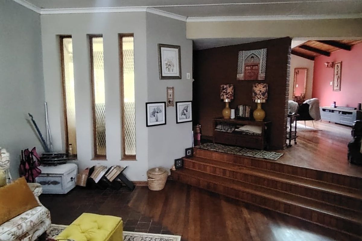 Spacious living area featuring a raised platform, hardwood and terracotta flooring, and unique vertical slit windows with exposed timber ceiling beams.
