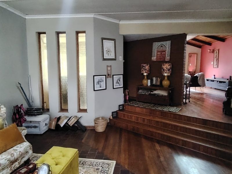Spacious living area featuring a raised platform, hardwood and terracotta flooring, and unique vertical slit windows with exposed timber ceiling beams.