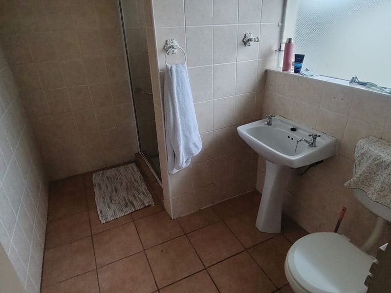 A functional bathroom featuring a pedestal basin, toilet, and a shower enclosure with neutral ceramic wall and floor tiling.