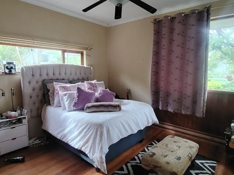 A bedroom featuring polished hardwood flooring, timber wall paneling, and a central ceiling fan.