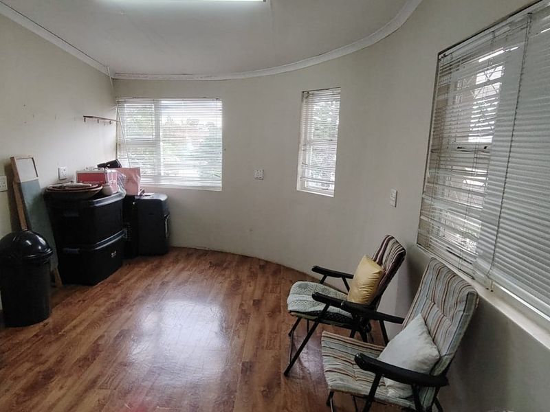 A living area featuring laminate flooring, curved wall design, and multiple windows with venetian blinds, offering a blank canvas for potential interior updates.