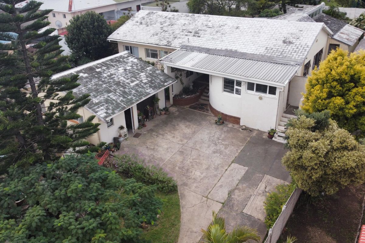 Aerial view of a residential property featuring a large concrete driveway, covered patio area, and a main dwelling with a weathered tiled roof.