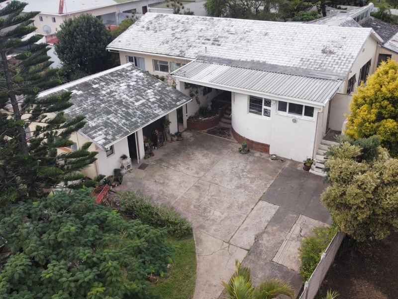 Aerial view of a residential property featuring a large concrete driveway, covered patio area, and a main dwelling with a weathered tiled roof.