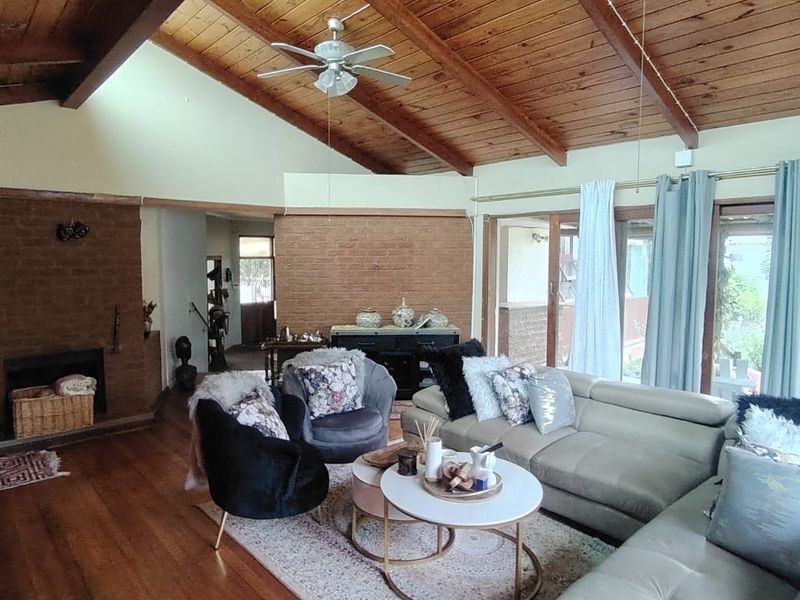 Spacious living room featuring high vaulted timber ceilings, exposed brick fireplace, hardwood flooring, and large sliding glass doors providing natural light.