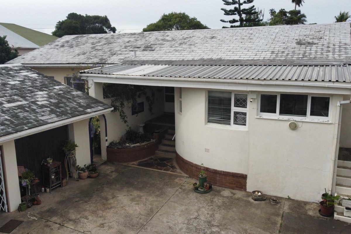 Rear exterior view of the property featuring a concrete driveway, covered patio area, and weathered roof shingles requiring maintenance.