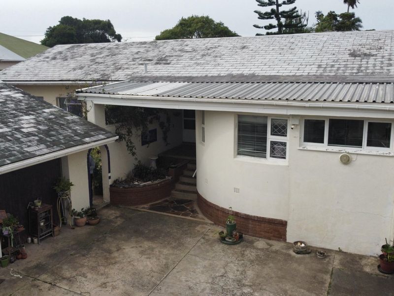 Rear exterior view of the property featuring a concrete driveway, covered patio area, and weathered roof shingles requiring maintenance.