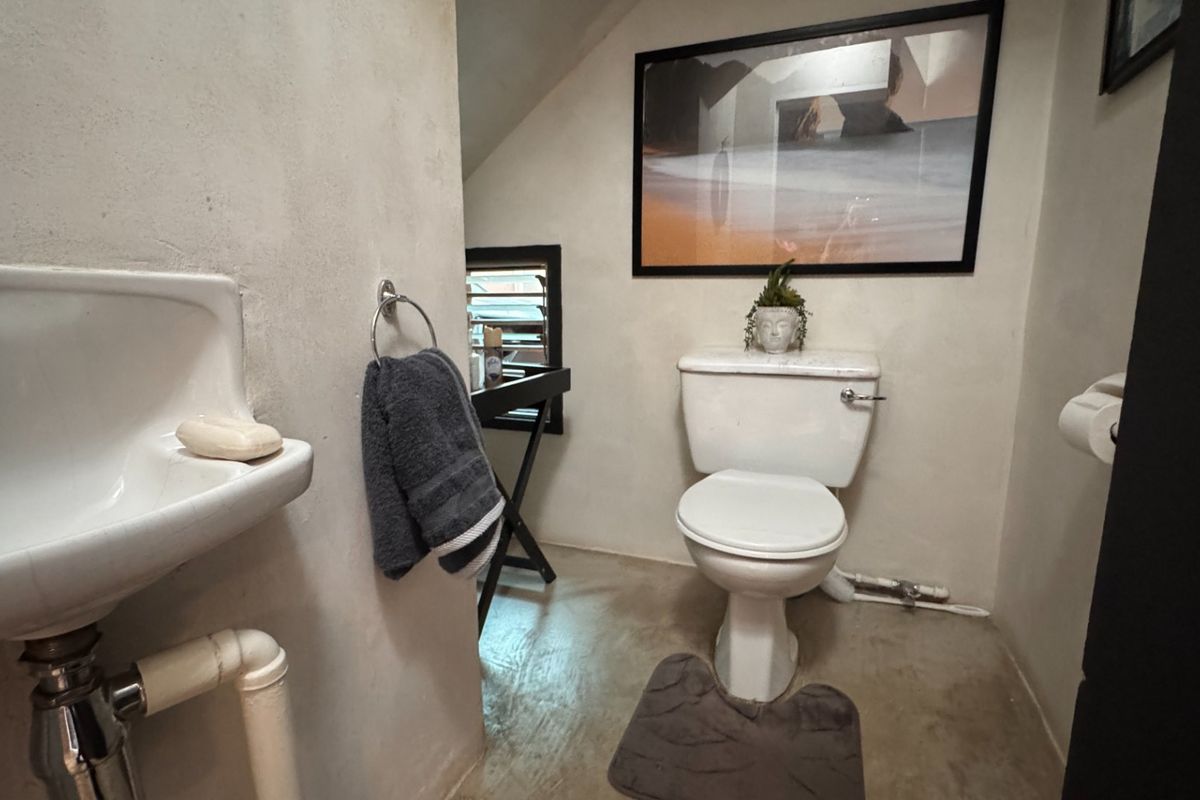 A compact bathroom featuring a wall-mounted basin and a standard toilet, finished with simple wall surfaces and concrete-style flooring.