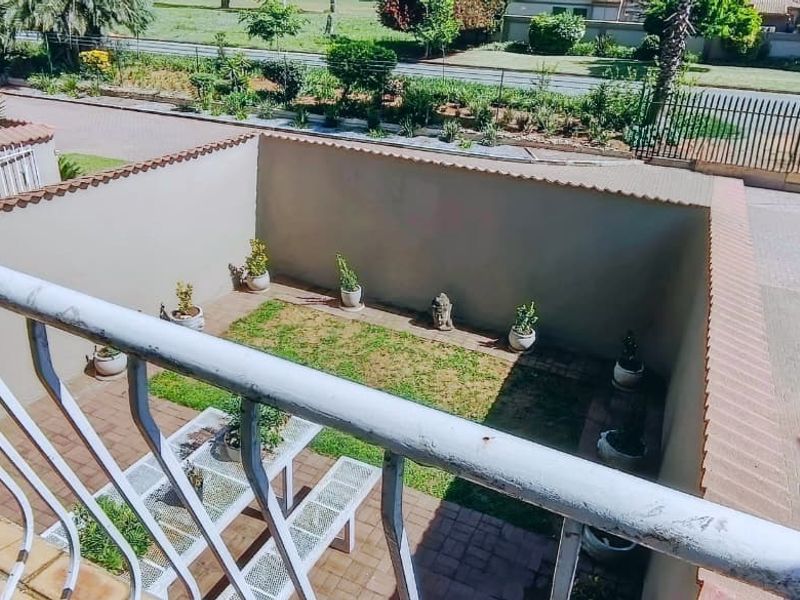 An elevated view of a private rear courtyard featuring a paved area, small lawn, and perimeter wall, viewed from an upper-level balcony.