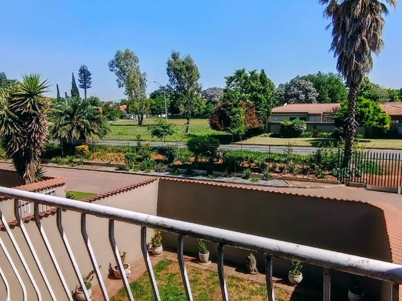 An elevated balcony view overlooking the property's paved driveway, perimeter wall, and surrounding landscaped garden area.