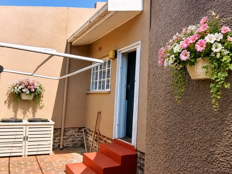 A rear courtyard area featuring brick paving, painted concrete steps, security-barred windows, and a wall-mounted clothesline.