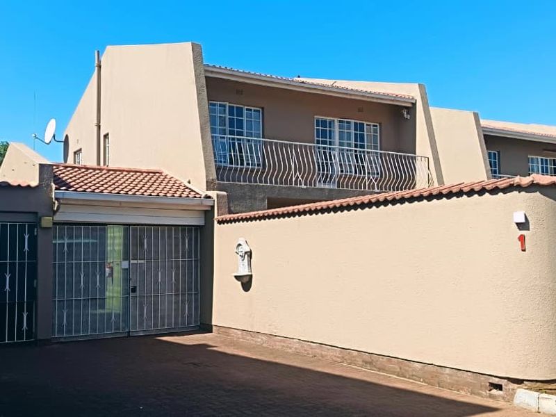 Front elevation of a townhouse featuring a paved driveway, secure gated entrance, and an upper-level balcony with metal railings.