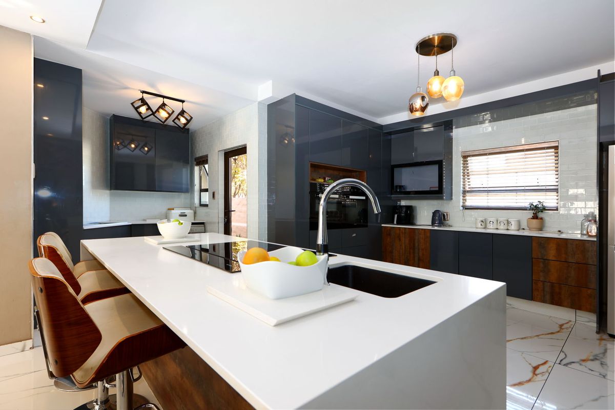 Modern kitchen featuring a large central island with quartz countertops, high-gloss cabinetry, integrated appliances, and stylish pendant lighting with marble-look flooring.
