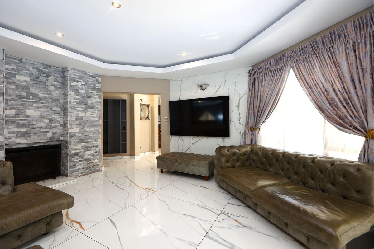 Spacious living room featuring a stone-clad fireplace, marble-effect feature wall, polished tiled flooring, and recessed ceiling lighting.