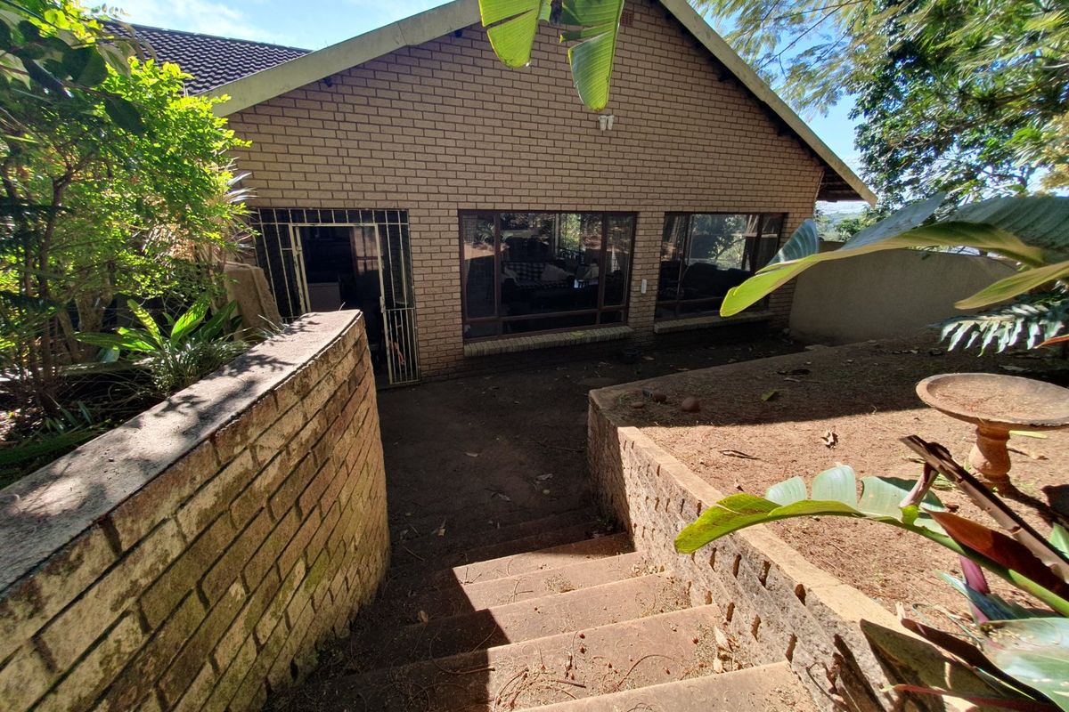 Rear view of a brick house featuring large windows, a security gate, and concrete stairs leading down to the garden area.