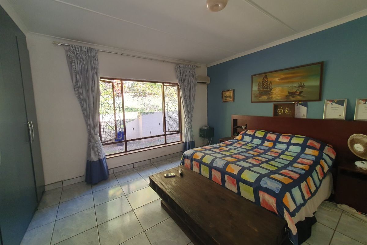 Spacious bedroom featuring tiled flooring, a built-in wardrobe, and an air conditioning unit, with large windows providing natural light and security bars.