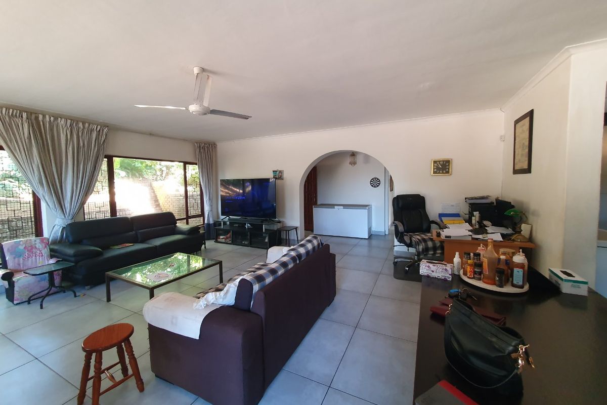 Spacious living area featuring tiled flooring, a ceiling fan, and an open archway leading to an adjacent space with large windows providing natural light.