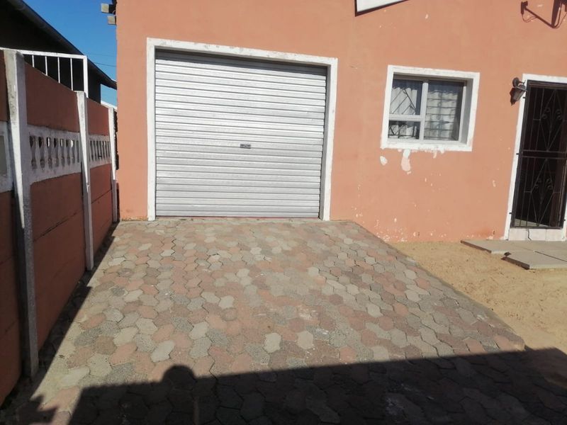 Exterior view of a single garage with a roller shutter door, paved driveway, and precast boundary walling.