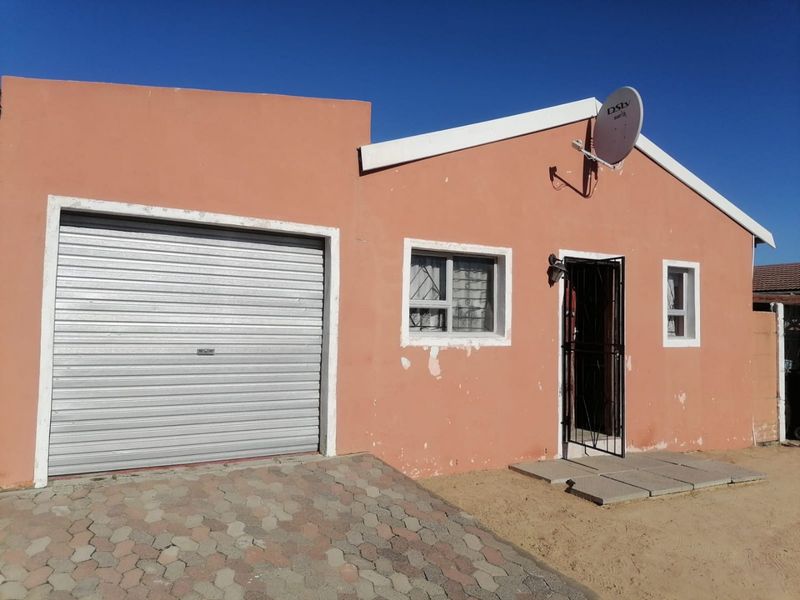 Front elevation of a single-story house featuring a roller garage door, paved driveway, and security features including bars and a gate.
