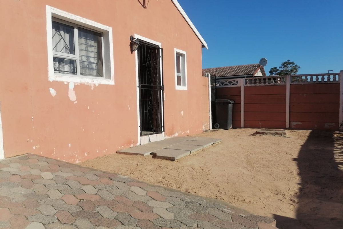 Rear exterior view of the house featuring a paved area, security gate, and perimeter walling, requiring some exterior maintenance and landscaping.