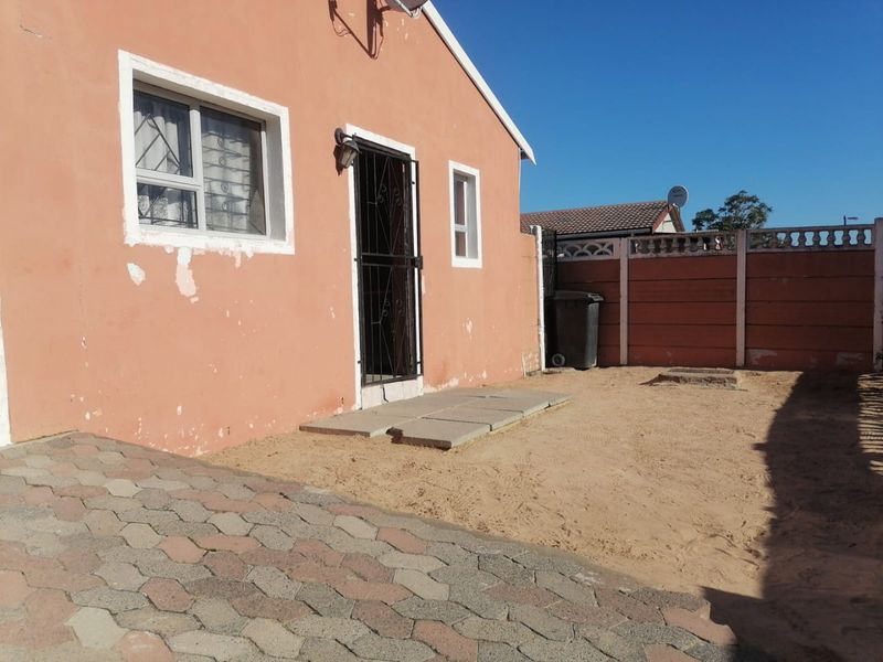 Rear exterior view of the house featuring a paved area, security gate, and perimeter walling, requiring some exterior maintenance and landscaping.