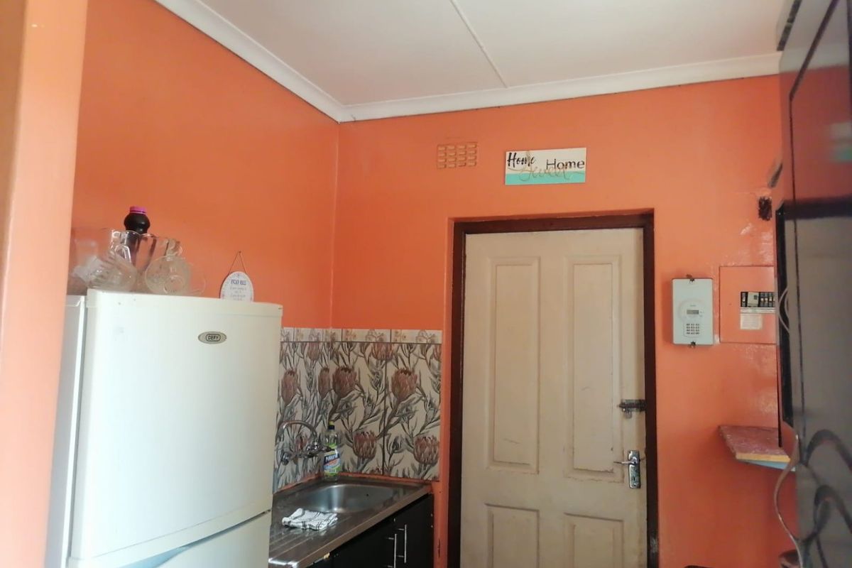 A compact kitchen area featuring a stainless steel sink, tiled backsplash, and built-in cabinetry, finished with bright orange wall paint.