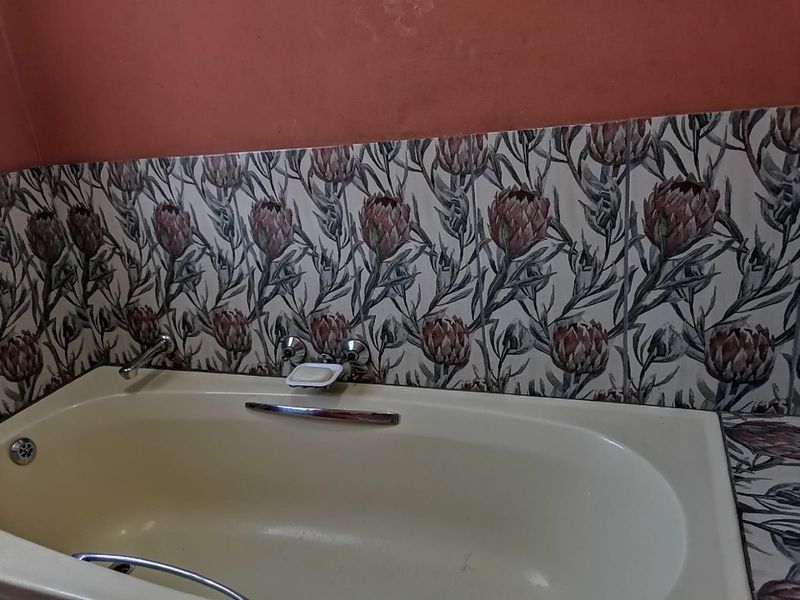 A bathroom featuring a built-in bathtub with floral patterned wall tiles and chrome fixtures.