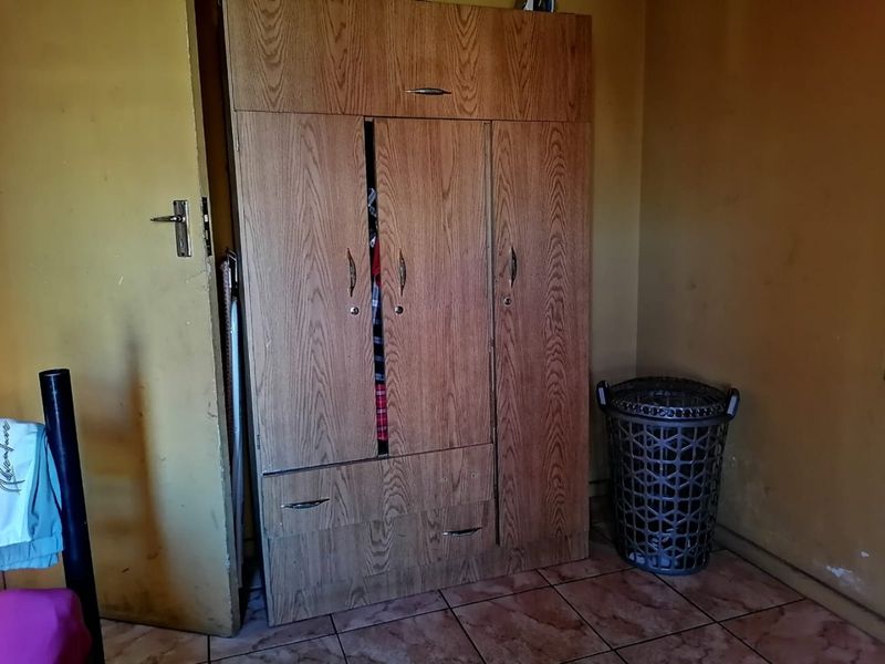 A bedroom featuring a built-in wooden wardrobe and tiled flooring, requiring cosmetic updates to the wall finishes.