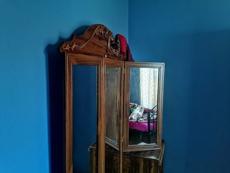 A bedroom corner featuring blue painted walls and a wooden vanity mirror unit.