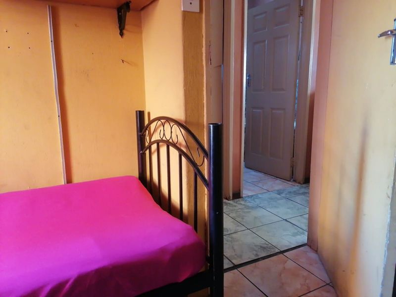 A bedroom featuring tiled flooring and access to an adjacent hallway, showing signs of wear on the wall surfaces.