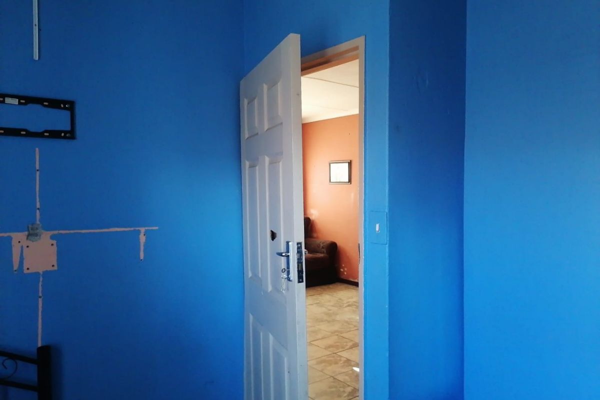 A bedroom interior featuring blue painted walls with visible surface damage and a doorway leading to an adjacent room.