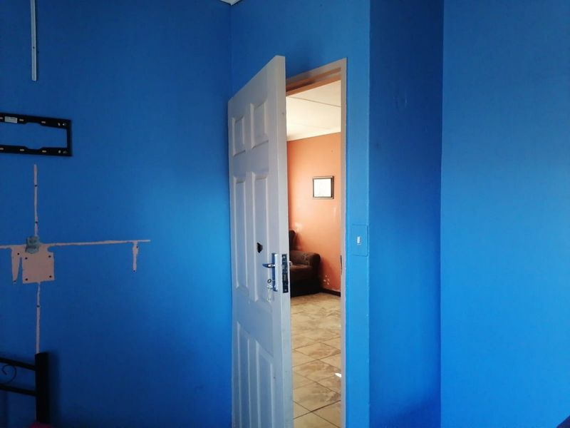 A bedroom interior featuring blue painted walls with visible surface damage and a doorway leading to an adjacent room.