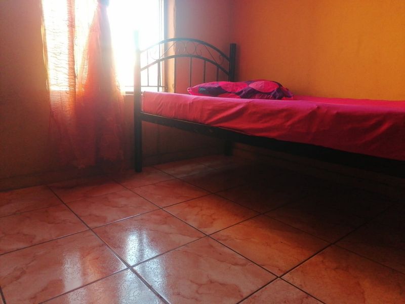 A simple bedroom featuring tiled flooring and natural light from a side window.