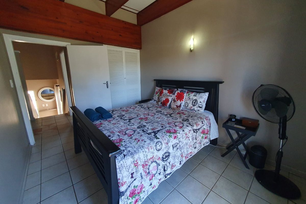 A bedroom featuring exposed timber ceiling beams, tiled flooring, and built-in louvered closet doors, with an adjacent hallway view.